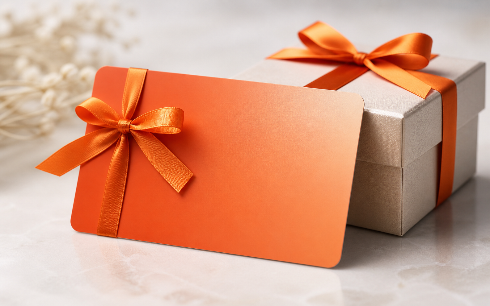 Eine leere orangefarbene Geschenkkarte mit einem Satinband neben einer elegant verpackten Geschenkbox auf einer sauberen, hellen Oberfläche